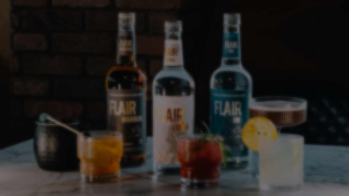 Three bottles of FLAIR Gin on a marble countertop with several prepared cocktails in front of them, set against a dark brick wall background.