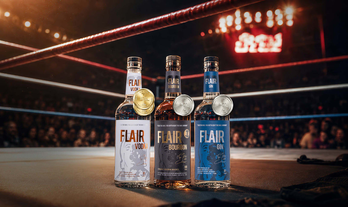 Three bottles of FLAIR Vodka lined up in a boxing ring, with a gold, silver, and bronze medal hanging from the necks. The background shows a blurred boxing arena with lights and a crowd.