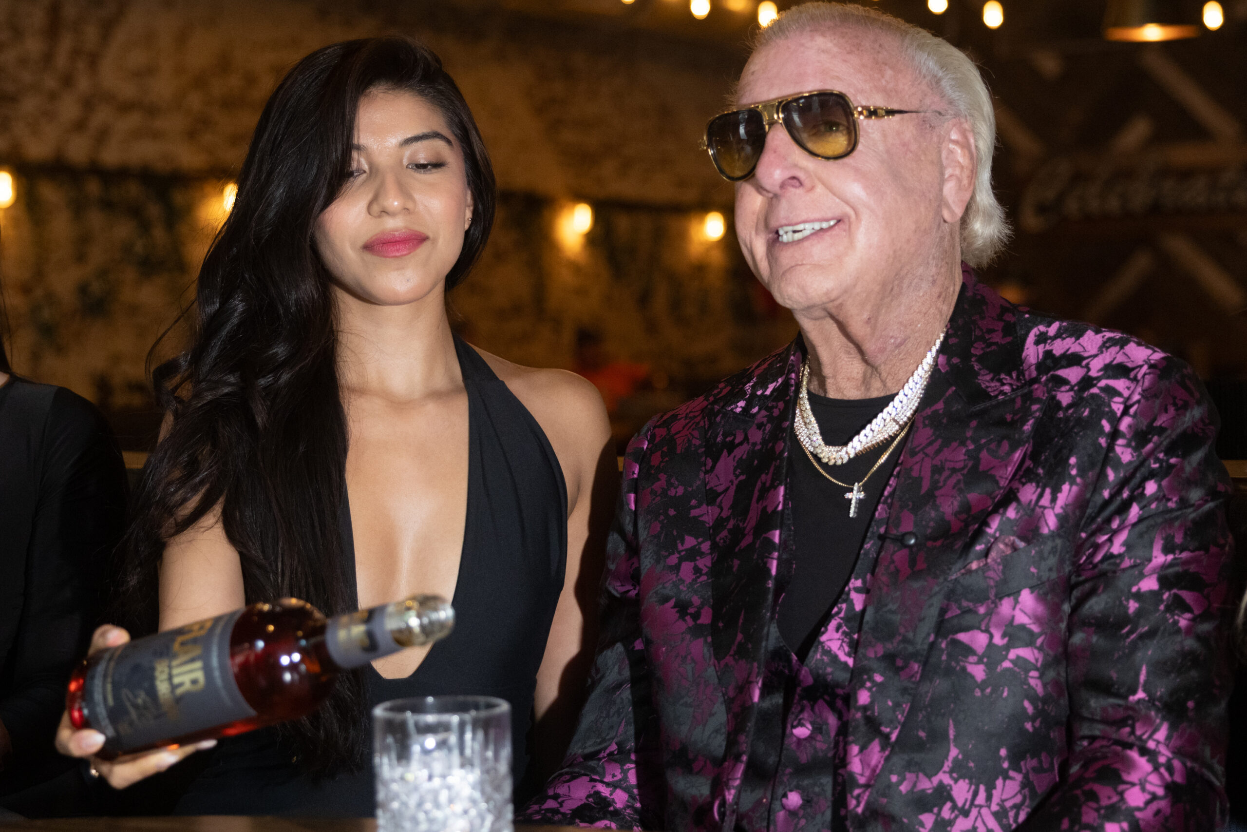 A lady pours Ric Flair a glass of hsi signature Flair Spirits bourbon.